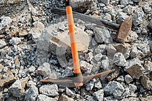 Geological pick with orange handle on the stones next to old hammer