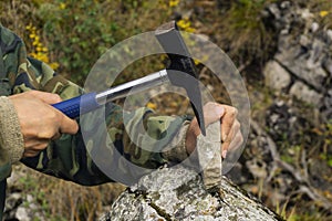 Geologist examines a mineralogical sample with the help of a geological hammer