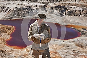 Geologist examines a sample of mineral in the desert against the background of a salt lake