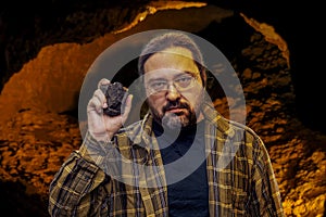 A geologist man in clean clothes with glasses holds in his hand a piece of coal