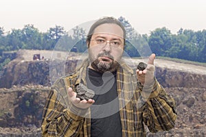 A geologist man in clean clothes with glasses holds in his hands a two pieces of coal