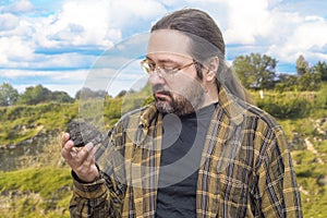 A geologist man in clean clothes holds in his hand a piece of coal