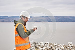 Geologist or mining engineer examines a sample of a mineral from a talus on a river bank