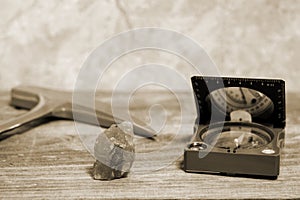 A geologist`s hammer, a compass, and a mineral interspersed with iron ore are laid out on a wooden table.