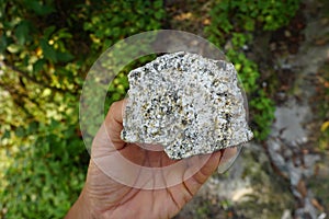 Geologist`s hand is holding a specimen of plutonic granite rock.