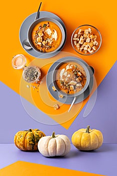 Geometric composition with pumpkin soup with cream, seeds and toasts on orange and violet backgroumd.
