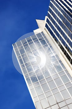 Geometric glass windows on a skyscraper with sun reflecting a lens flare against a blue sky background from below