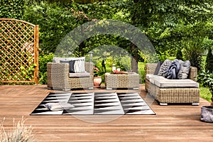 Geometrical rug and rattan furniture set on a terrace in a garden full of trees