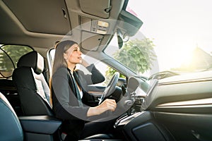 Georgeous young business woman in black suit looking in the rearview mirror of a car. Young smiling businesswoman