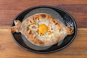 Georgian cuisine. Ajara khachapuri with egg on black plate on wooden background