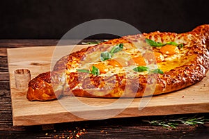 Georgian cuisine. Big khachapuri with 5 egg yolks, on a wooden board. A dish in a restaurant for a large company of people.