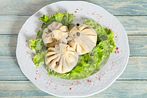 Georgian dumplings Khinkali with meat, lettuce and pepper on white plate on wooden table