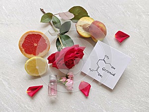 Geraniol, chemical formula with rose essential oil in a glass bottle, fresh citrus fruit, peach, rose flowers and petals
