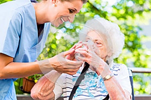 Geriatric nurse giving glass of water to senior woman photo