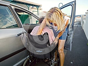 A geriatric nurse helps a frail elderly woman from a car into a wheelchair