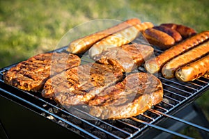 German Bratwurst sausages and marinated pork neck steak meat roasting with smoke on foldable charcoal BBQ barbecue grill in garden