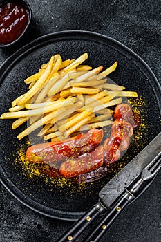 German currywurst Sausages with French fries on a plate. Black background. Top view