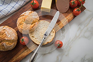 German fine veal liver sausage spread with two crispy bread rolls buns, tomatoes, butter and knife on wooden board, kitchen towel