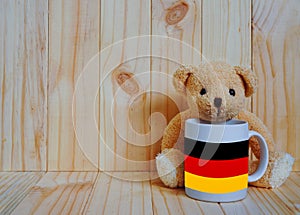 German flag on a coffee cup with teddy bear and wooden background.