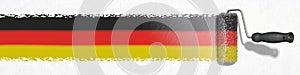 German flag colors. Paint roller paints black, red, golden color stripes on white wall