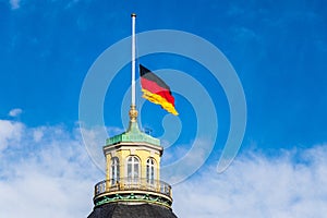 German Flag at Halfmast, auf Halbmast, on tower roof of Castle Karlsruhe. Blue sky in background. In Baden-WÃ¼rttemberg, Germany