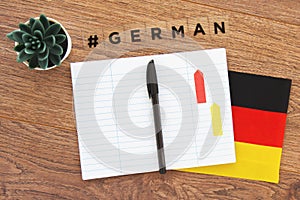 German flag, notebook, pen and inscription hashtag german on a wooden desktop, foreign language concept