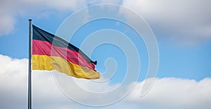 German flag waving on flagpole. Cloudy blue sky background, copyspace, banner.