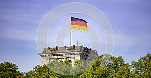 German flag waving on silver flagpole, Reichstag building in Berlin. Blue sky with clouds background