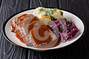 German food Sauerbraten - slowly stewed marinated beef with gravy with potato dumplings and red cabbage close-up on a plate. photo