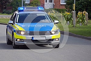 German police car on duty driving with flashing blue lights on through a rural suburb, inscription Polizei means police, copy photo