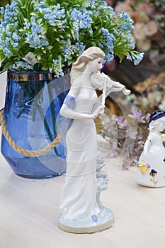 German porcelain figurine of a violinist girl. Ceramic figurine of the violoncellist in retro style with blue flowers on the table