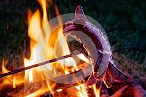 German sausage on metal skewer cooking on fire at night.