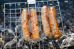 German sausages fried on a metal grill against the background of smoldering coals of the grill. Cooking barbecue