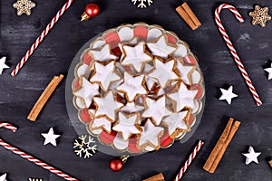 German star shaped glazed cinnamon Christmas cookies called `Zimtsterne` on striped plate surrounded by cinnammon sticks