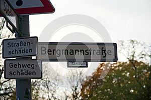 German Street Sign of Bergmannstrasse with additional Signs saying Roadway Damage and Sidewalk Damage