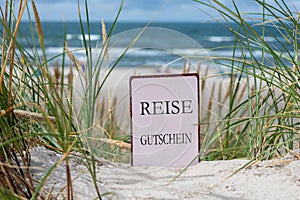 The German text \'Reise Gutschein\' (travel voucher) in the sand dunes at the beach