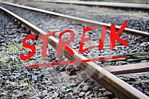 German text Streik meaning strike over rusty metal railway tracks and brackets in a ballast bed, selected focus