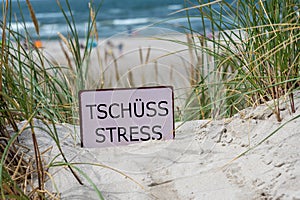 The German text \'Tschuess Stress\' (goodbye stress) in the sand dunes at the beach