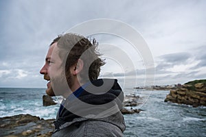 German Traveler on the rocks near the sea looking far away at horizon. Rocky Atlantic Ocean Coastline and Stormy Weather