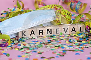 German word KARNIVAL on wooden blocks under a face mask with confetti and streamers