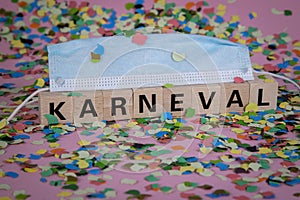 German word KARNIVAL on wooden blocks under a face mask with confetti and streamers