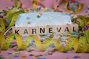 German word KARNIVAL on wooden blocks under a face mask with confetti and streamers