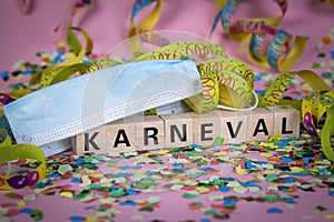 German word KARNIVAL on wooden blocks under a face mask with confetti and streamers