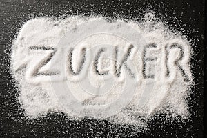 German word Zucker, meaning sugar, written in spilled out sugar crystals on a dark slate, high angle view from above photo