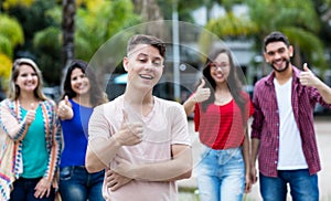 German young adult showing thumb up with group of friends