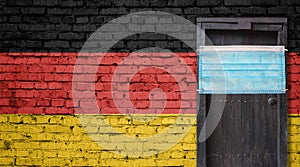 Germany flag painted on brick wall and closed door with medical mask protected