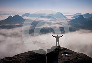 Gesture of triumph. Happy hiker in black. Tall man on the peak of sandstone rock in national park Saxony Switzerland above valley