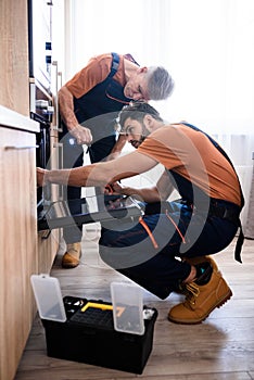 Get the best Handyman service. Full length shot of two repairmen, workers in uniform examining oven using screwdriver