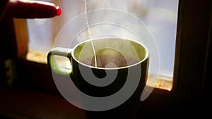 Get a cup of hot water with tea bag A red, back and forth, to brew a delicious tea, against the window with a bright sun