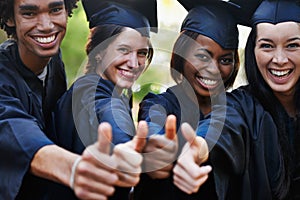 Get educated. A group of smiling college graduates giving the thumbs up at graduation.